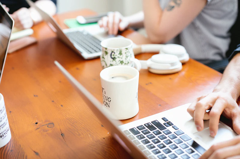 Two people talking over coffee with laptops open on a wooden table