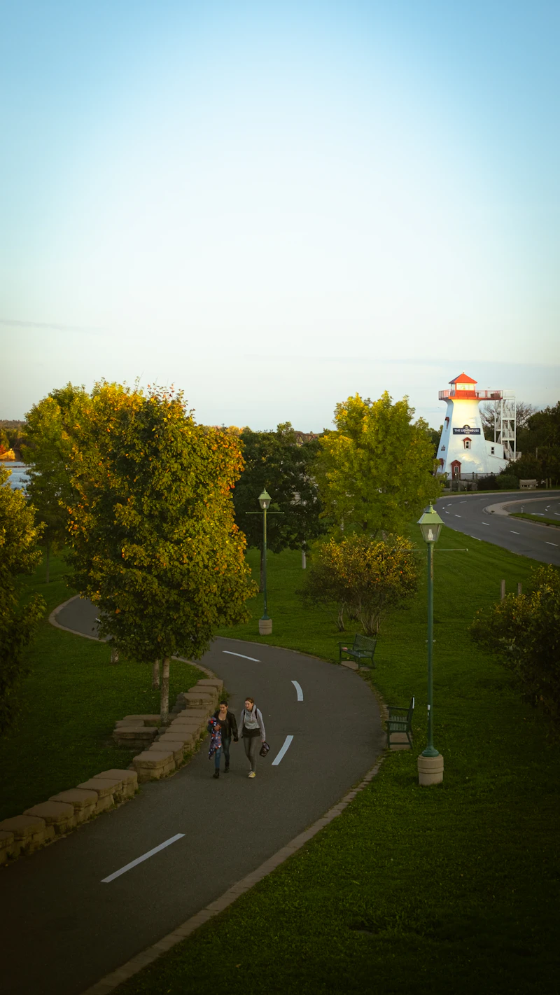 People walking the riverfront trail in Fredericton on an autumn evening, with the lighthouse ahead
