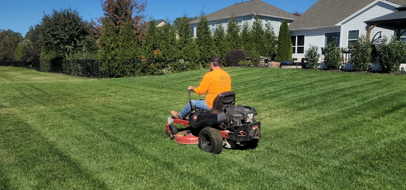 A lawn care worker mowing a large green lawn on a ride-on mower